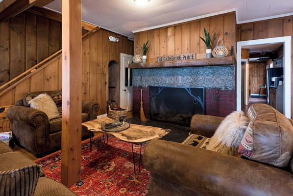 A cozy living room with a fireplace, wooden walls, and comfortable seating. - Pleasant Point Inn (Lovell)