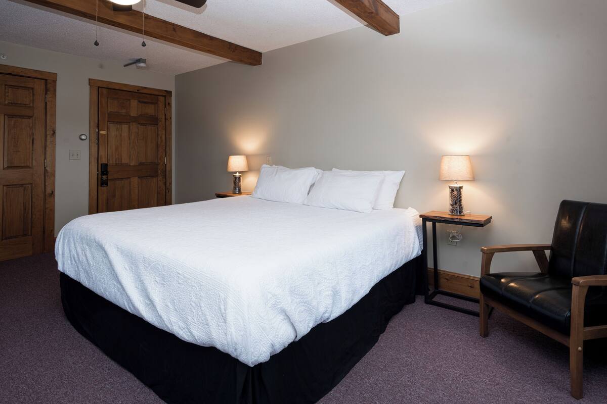 Un dormitorio con una cama grande, dos mesitas de noche con lámparas, una silla de madera y puertas de madera.