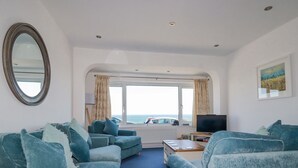 Una sala de estar con dos sofás, una mesa de centro, un televisor y un ventanal con vistas al mar.