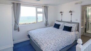 Un dormitorio con cama, ventana con cortinas, lámpara de noche y vista al mar.