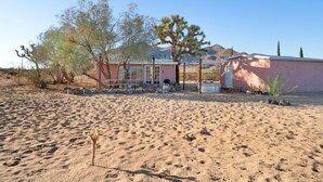 A desert landscape with a pink building, a small pool, and sparse vegetation. - Goat House - Bbq, Hammocks And Dark Skies! 1 Bedroom Home by RedAwning (Landers)