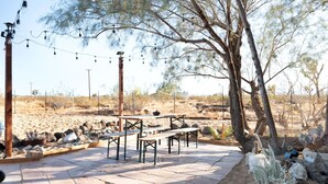 An outdoor patio area with stone flooring, picnic tables, and string lights. - Goat House - Bbq, Hammocks And Dark Skies! 1 Bedroom Home by RedAwning (Landers)