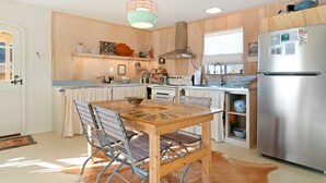 A kitchen with a wooden table, chairs, a hanging light fixture, a refrigerator, and a stove. - Goat House - Bbq, Hammocks And Dark Skies! 1 Bedroom Home by RedAwning (Landers)