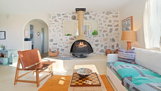 A living room with a stone wall, a fireplace, a sofa, a chair, and a table with a bowl. - Goat House - Bbq, Hammocks And Dark Skies! 1 Bedroom Home by RedAwning (Landers)