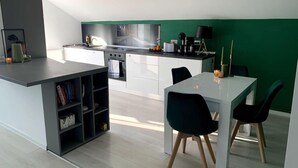 A modern kitchen with white cabinets, a black countertop, and a green accent wall. There is a dining area with two chairs and a table. - Spacious 3 Bed Apartment Cluj Floresti Near Vivo (Floresti)