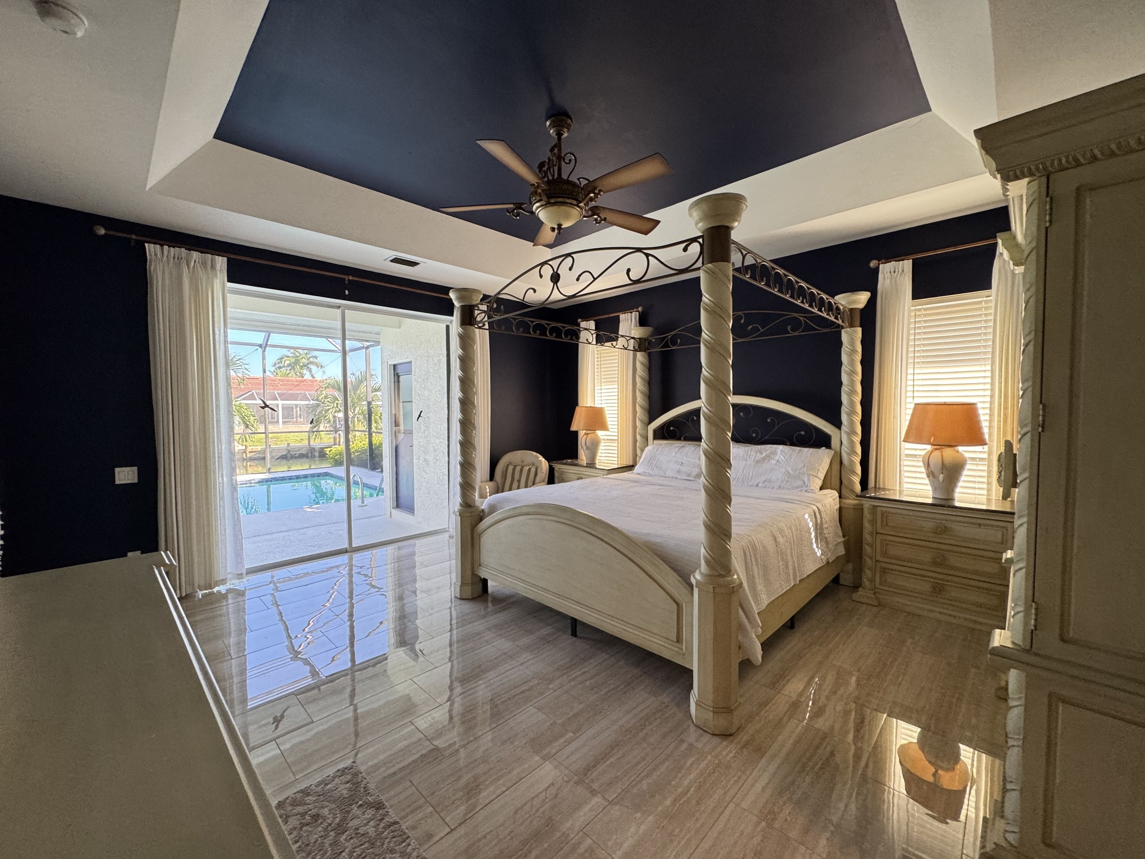 Une chambre à coucher avec un lit à baldaquin, un ventilateur de plafond et une vue sur une piscine.