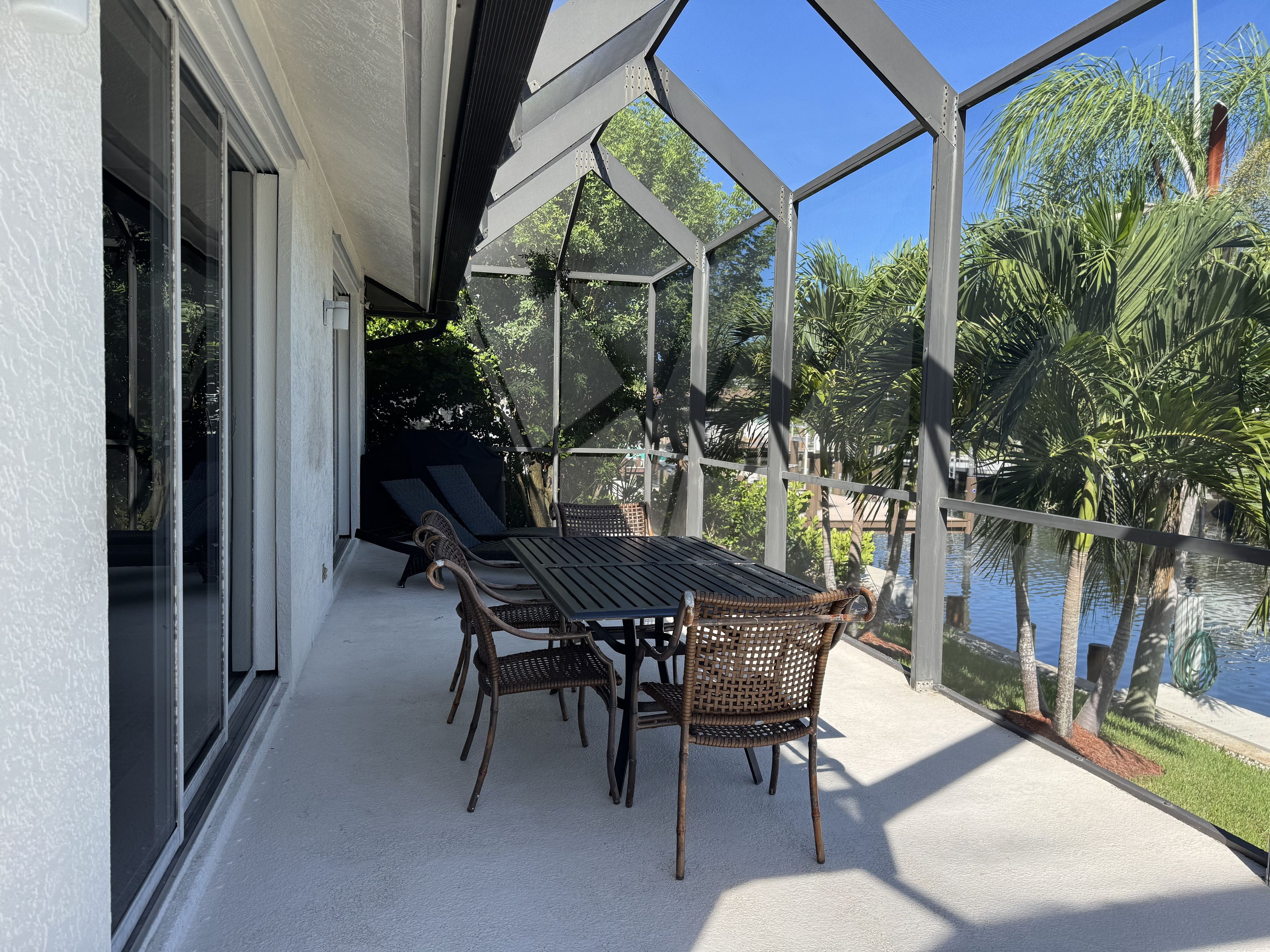 An outdoor patio with a table and chairs, overlooking a body of water and surrounded by greenery.