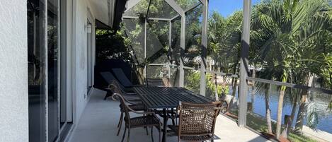 An outdoor patio with a table and chairs, overlooking a body of water and surrounded by greenery.