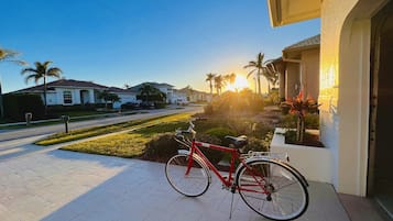 Una bicicleta roja estacionada en un camino pavimentado, con vista a una calle residencial y casas al fondo.
