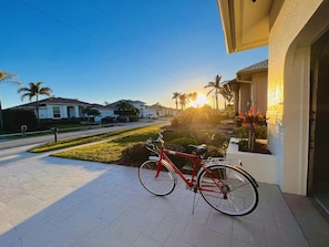 A red bicycle parked on a paved driveway with a view of a residential street and houses in the background. - Lighthouse 1124 3 Bedroom Home by RedAwning (Marco Island)