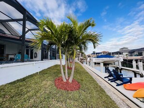 A modern waterfront property with a covered patio, lounge chairs, and a marina with boats. - Lighthouse 1124 3 Bedroom Home by RedAwning (Marco Island)