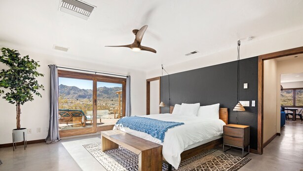 A modern bedroom with a large bed, a ceiling fan, and a view of mountains through the sliding glass door. - Dreamspace - Hot Tub, Fire Pit, 5 Min. To Park 2 Bedroom Home by RedAwning (Joshua Tree)