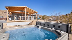 A hot tub with a wooden deck and a covered area, surrounded by a desert landscape. - Dreamspace - Hot Tub, Fire Pit, 5 Min. To Park 2 Bedroom Home by RedAwning (Joshua Tree)