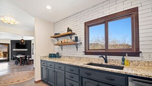 A modern kitchen with dark cabinets, a granite countertop, and a large window. - Dreamspace - Hot Tub, Fire Pit, 5 Min. To Park 2 Bedroom Home by RedAwning (Joshua Tree)