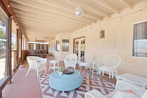 A covered outdoor patio with wicker furniture, a hanging disco ball, and a patterned floor. - Euphorbia House - Fire Pit, Ping Pong, Tether Ball & Dark Skies 3 Bedroom Home by RedAwning (Yucca Valley)