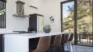 Una cocina moderna con una isla central, taburetes de bar y un amplio ventanal con vistas al exterior.