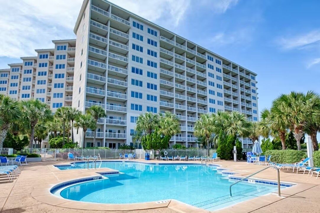 Ein Hotel mit mehreren Etagen, einem Schwimmbad und Palmen.