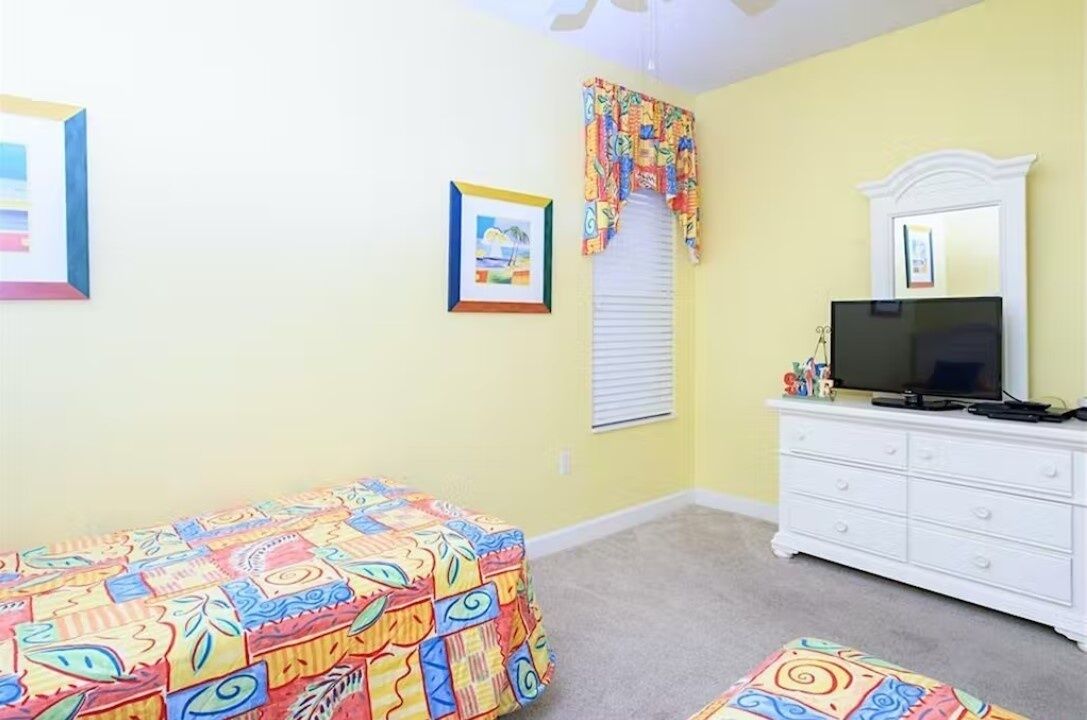 Un dormitorio con cama, cómoda, televisor y ventana con persianas.