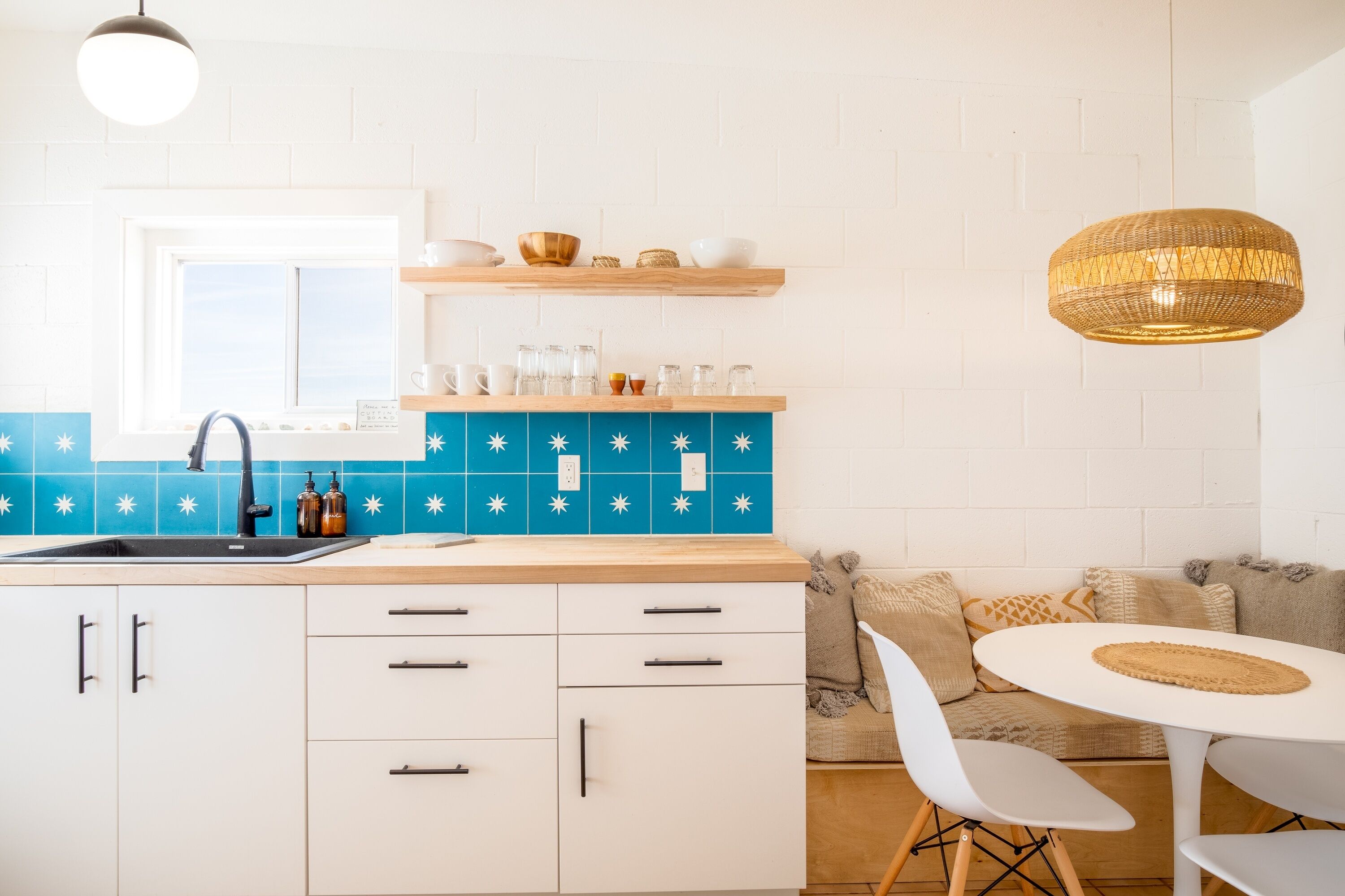 Una cocina moderna con armarios blancos, salpicadero azul y comedor con mesa redonda y sillas blancas.