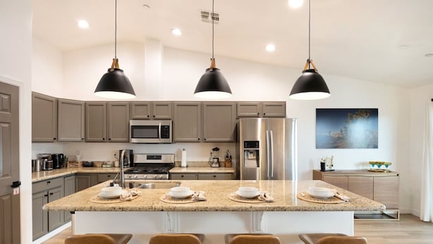 A modern kitchen with a central island, bar stools, stainless steel appliances, and pendant lighting. - Alana House - Pool, Hot Tub, Bbq, Fire Pit + Walk To Hikes! 4 Bedroom Home by RedAwning (Joshua Tree)