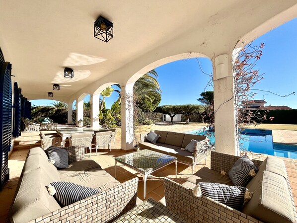Un patio al aire libre con mobiliario de mimbre, una piscina y una vista despejada del paisaje circundante.