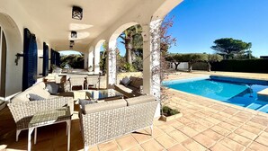 An outdoor patio with a pool, featuring a covered seating area with wicker furniture and a clear view of the pool.