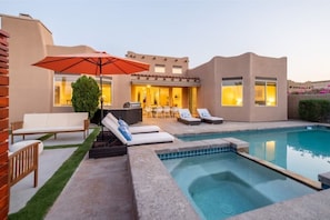 Un espace piscine extérieur moderne, doté de chaises longues, d’un barbecue et d’une terrasse avec une table et des chaises.