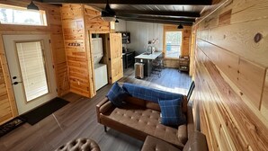 Ein gemütliches Blockhaushaus-Interieur mit Holzvertäfelungen, einer Couch mit blauen Kissen, einem Essbereich und einer Küchenzeile.