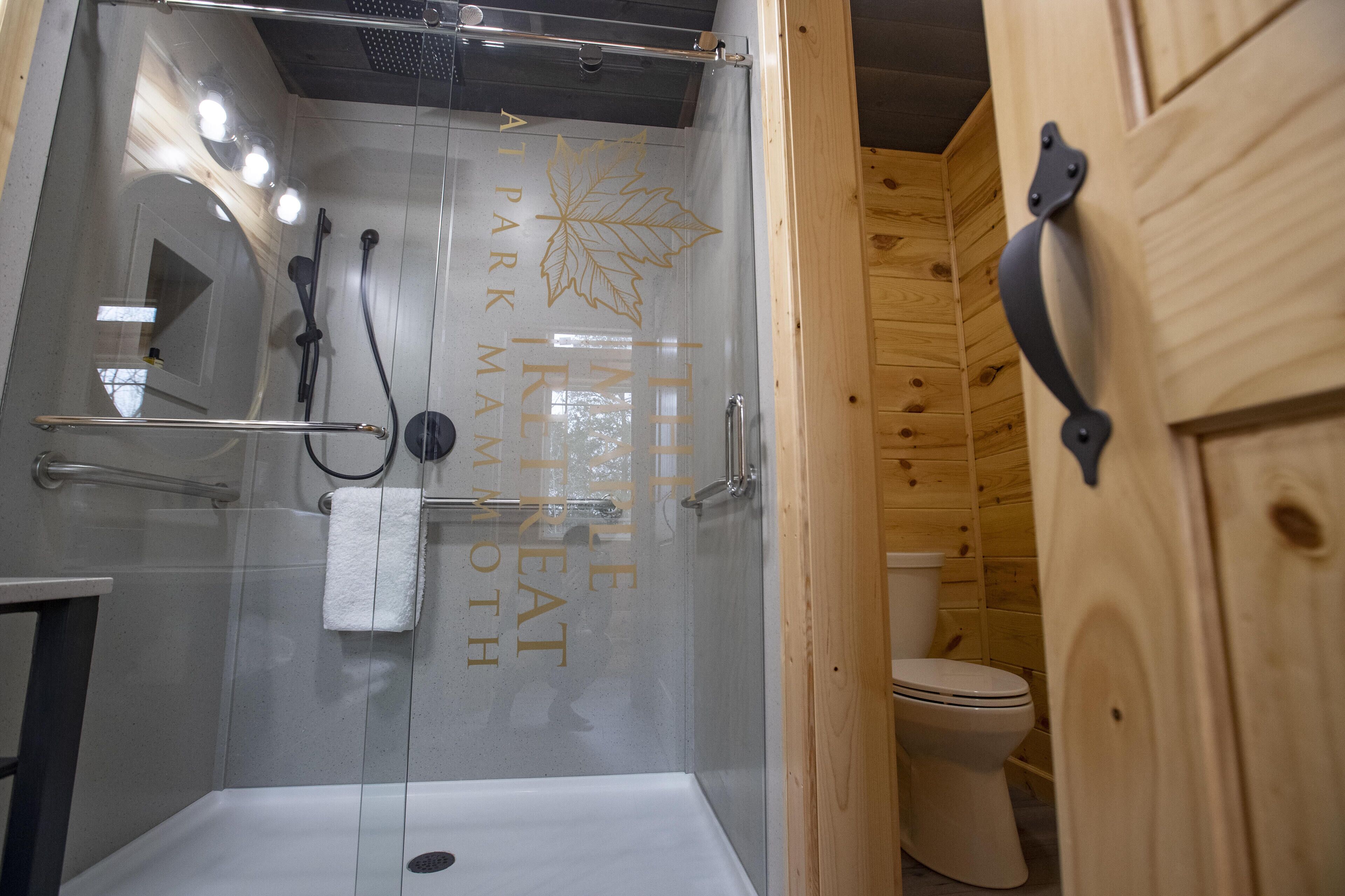 A glass-enclosed shower with a white bathtub, a towel rack, and a toilet in a wooden cabin-style bathroom.