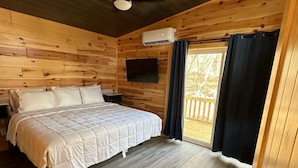 Ein Schlafzimmer einer Holzhütte mit einem Bett, einem Deckenventilator und einem Fenster mit Vorhängen.