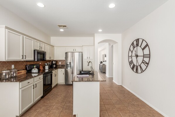 Kitchen features a central island with a sink and a refrigerator, microwave, and wall-mounted clock.