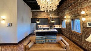 A modern kitchen with a brick wall, a large chandelier, and a cozy seating area with a patterned throw. - 1882 Lofts - 402-Downtown 2nd & Church (Nashville)