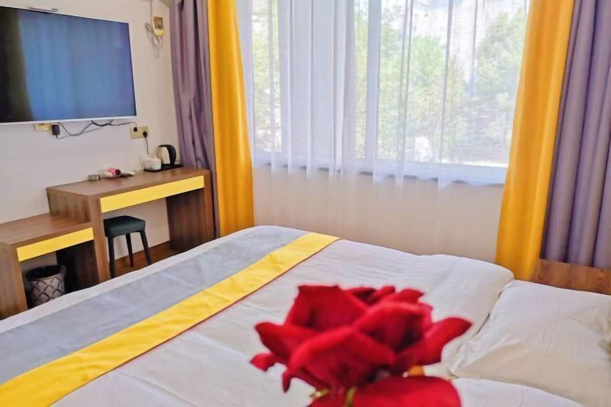 Una habitación de hotel con cama, escritorio, televisión y ventana con cortinas.