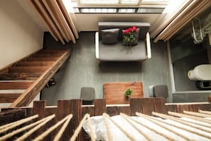 A modern interior with a staircase, a sofa with cushions, a small table with a plant, and a view of the outdoors through a skylight.