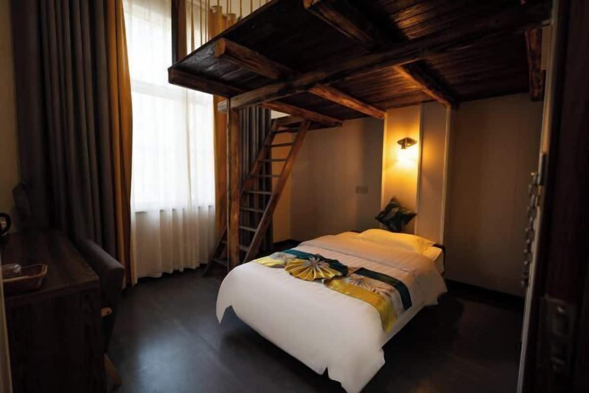 Un dormitorio con cama, escritorio, escalera y ventana con cortinas.