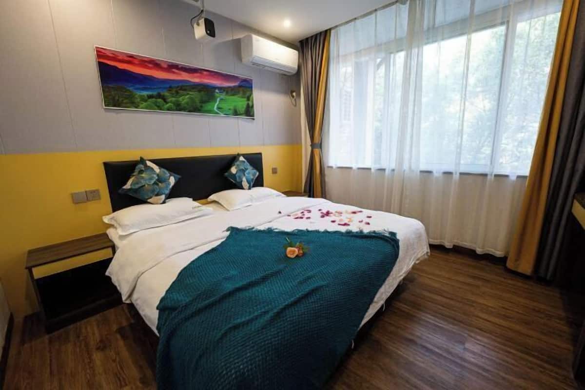 Habitación de hotel con cama, un cuadro en la pared y una ventana con cortinas.