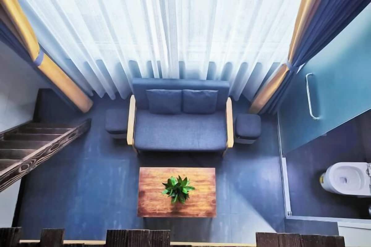 Una habitación compacta y moderna con un sofá, una pequeña mesa de madera con una planta, una escalera y un baño con inodoro.