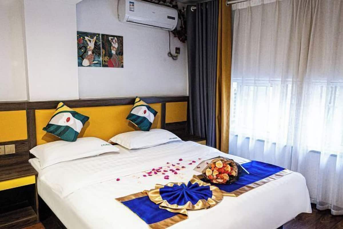 Una habitación de hotel con una cama, almohadas, un ramo de flores y una pared decorada con obras de arte.