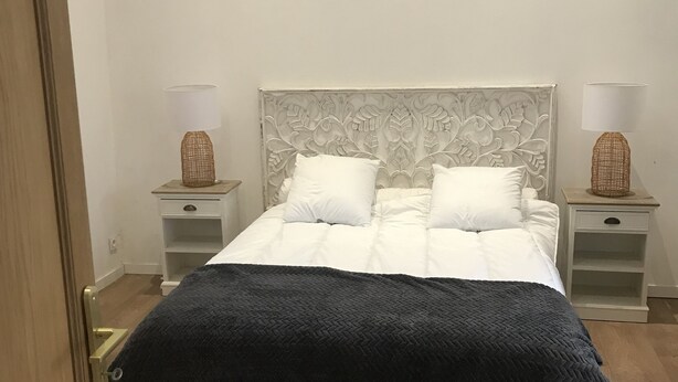 A bedroom with a bed, two bedside tables, a nightstand, a wooden door, and a white wall. - Renovated house with garage and 300 M2 of land,  (Condé-sur-Sarthe)