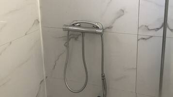 Ein Badezimmer mit weißen Marmorfliesen und einer Dusche inklusive Handbrause.