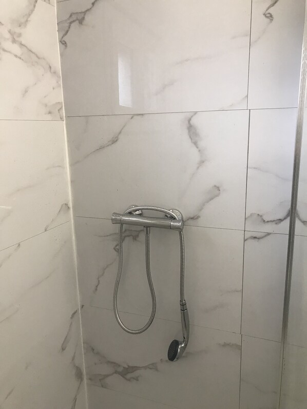 Ein Badezimmer mit weißen Marmorfliesen und einer Dusche inklusive Handbrause.