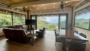 Uma sala de estar espaçosa com um amplo teto de madeira, uma TV de tela plana e uma mesa de jantar com cadeiras.
