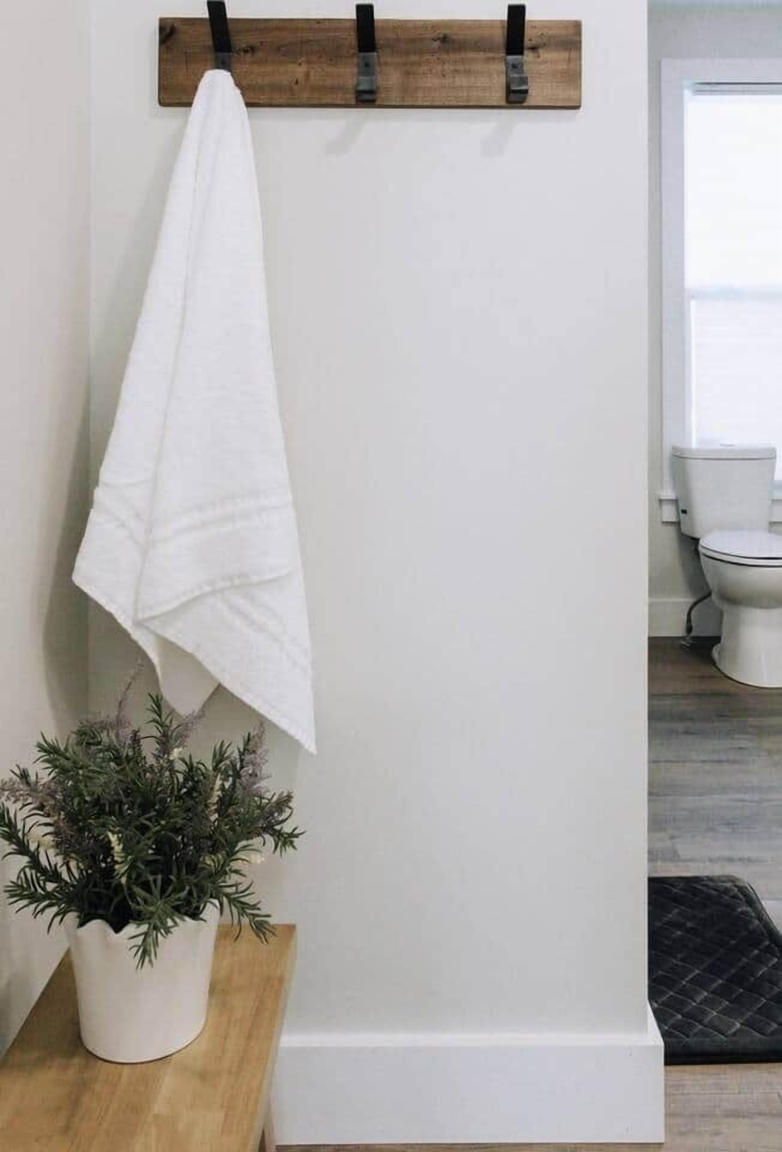 Una toalla blanca colgada en un perchero de madera, una planta en maceta sobre un taburete de madera y un inodoro blanco en un baño.