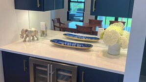 A modern kitchen with dark blue cabinets, a built-in refrigerator, and a dining area visible through a window.