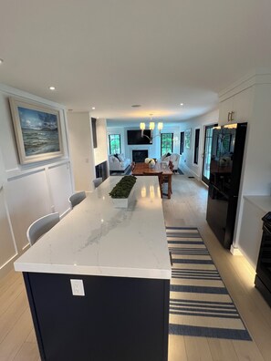 Een moderne keuken met een marmeren eiland, een eethoek met een houten tafel en een inbouwkoelkast.