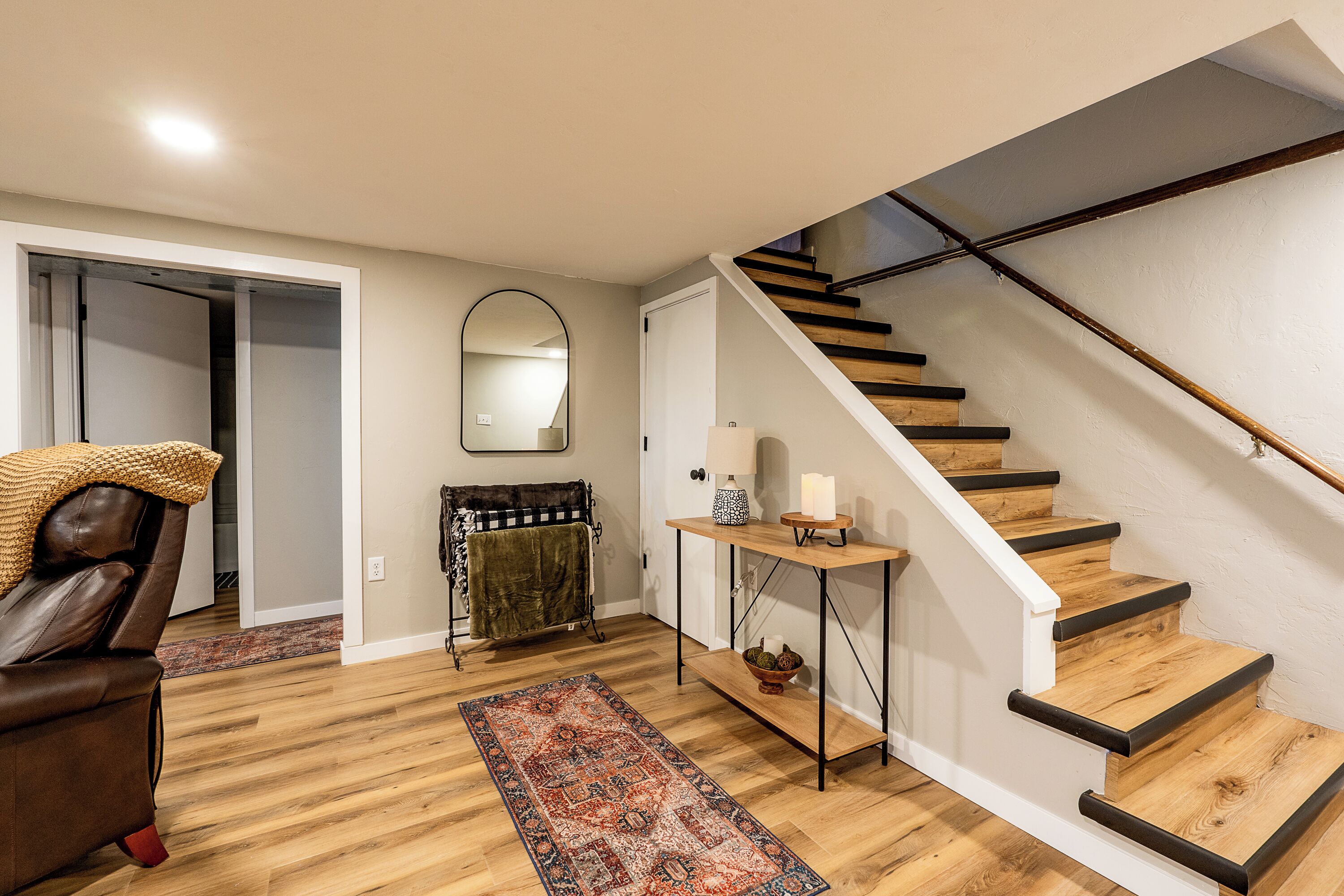A staircase with wooden steps and black handrails, a brown leather chair, a patterned rug, a small table with candles, and a mirror on the wall.