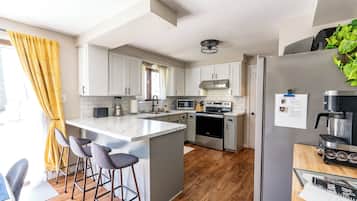 Een moderne keuken met witte kasten, een centraal eiland met barkrukken, een inbouwoven en een koelkast met een koffiezetapparaat.