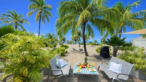 A tropical outdoor seating area with a table set for two, surrounded by palm trees and a sandy beach. - MOOREA Exceptional view of the Caribbean Sea, Swimming pool (Collectivité de Saint-Martin)