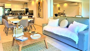 A modern living room with a grey sofa, a wooden coffee table, and a dining area with a white table and grey chairs. - MOOREA Exceptional view of the Caribbean Sea, Swimming pool (Collectivité de Saint-Martin)