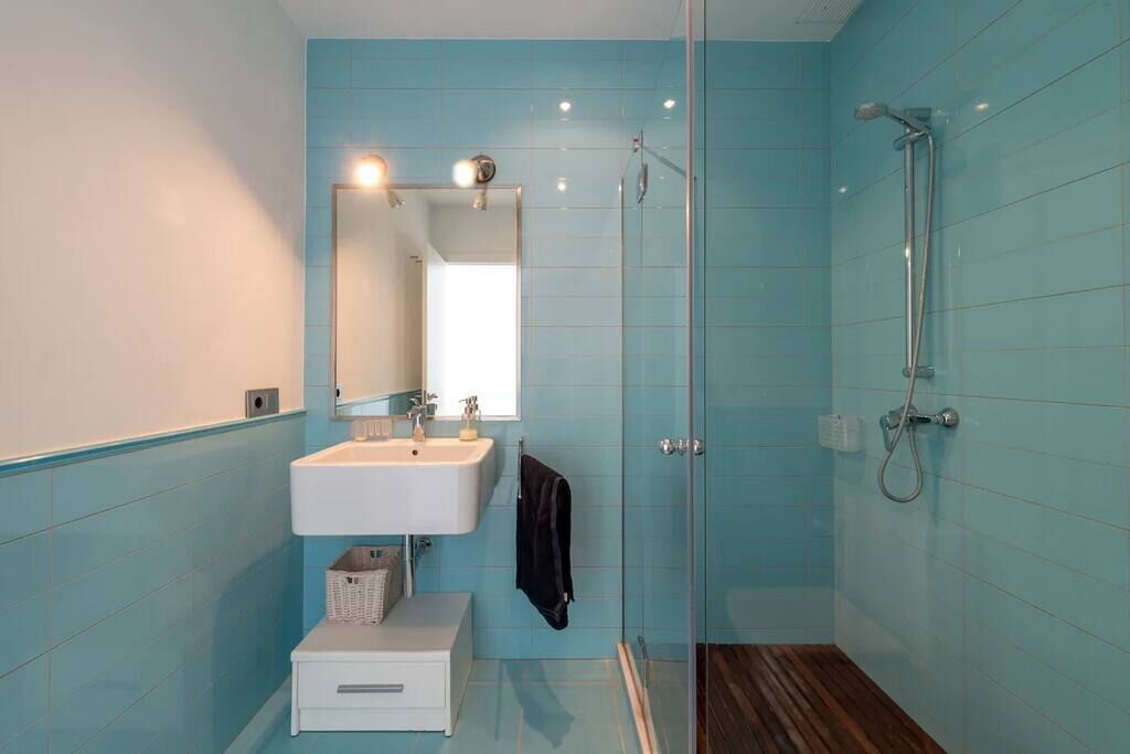 Een moderne badkamer met een douchecabine van glas, een witte wastafel en een spiegel erboven.